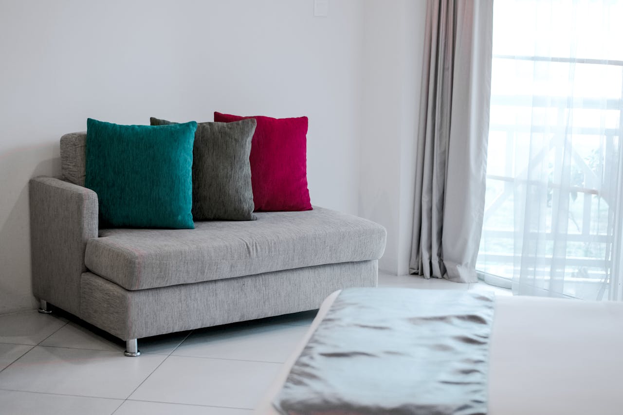 services-05 Simple modern interior featuring a grey sofa with vibrant colored cushions in a bright room.